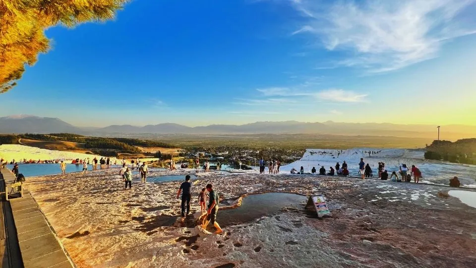 Travertine terraces of Pamukkale at sunset, with barefoot visitors and the Denizli plain in the background